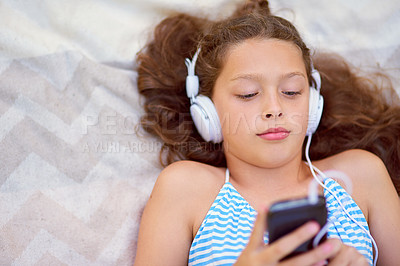Buy stock photo High angle shot of a young girl listening to music on her cellphone while lying on a blanket outside