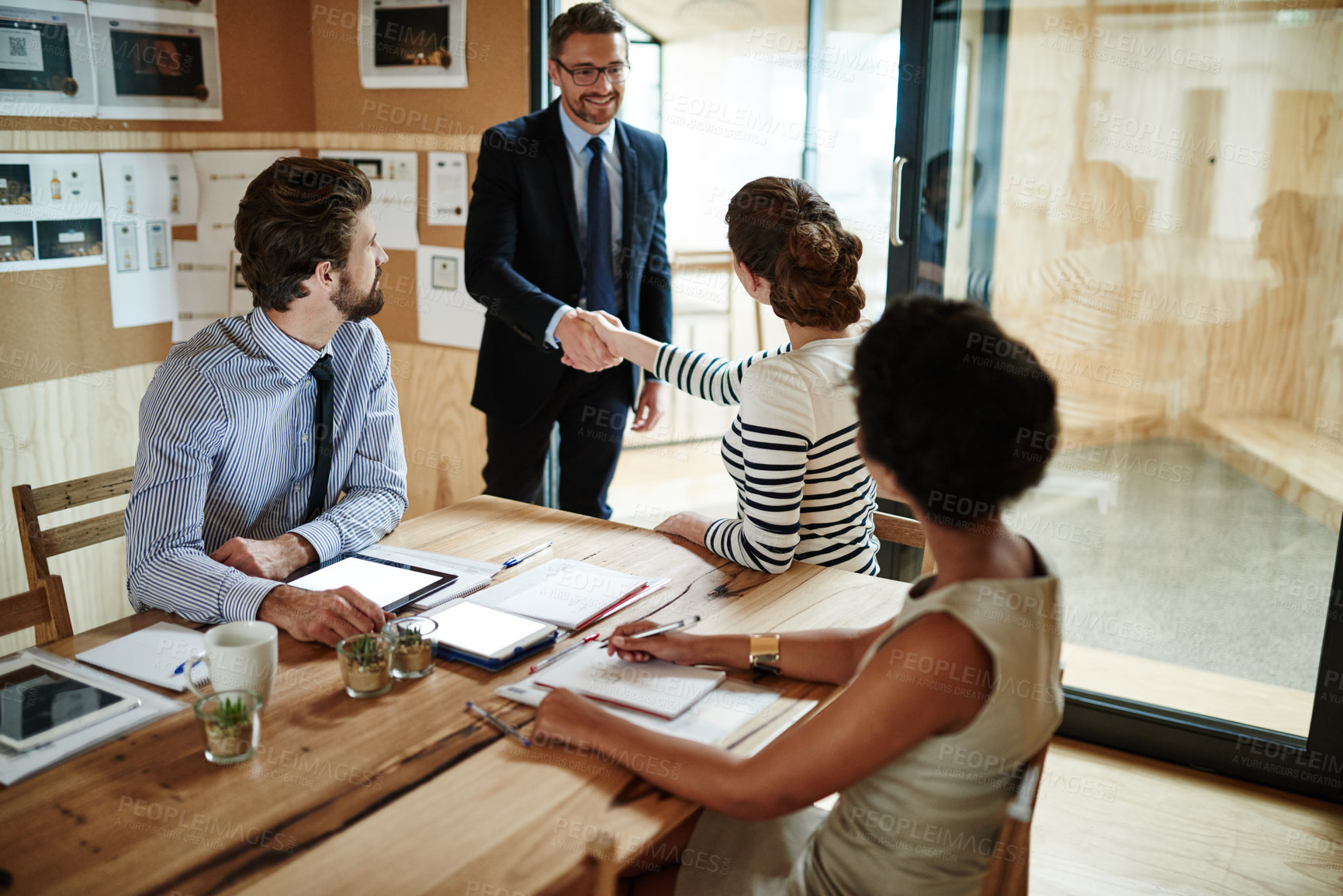 Buy stock photo Shot of two businesspeople shaking hands in an office while colleagues look on