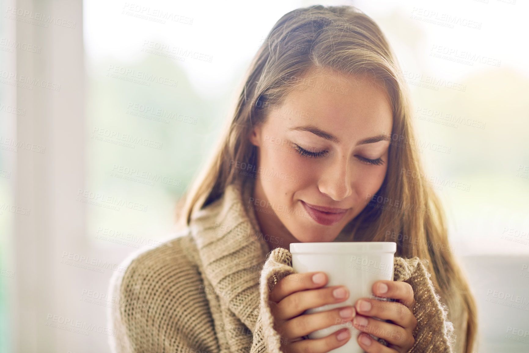 Buy stock photo Shot of a young woman enjoying a warm beverage at home