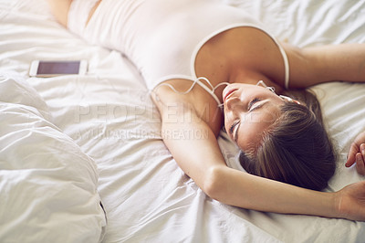 Buy stock photo Shot of a young woman listening to music while relaxing on her bed
