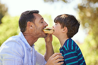 Buy stock photo Shot of a father and son biting into a sandwich at the same time