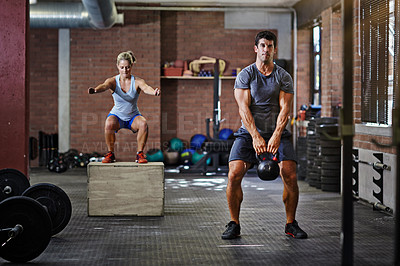 Buy stock photo Shot of two people working out with kettlebells in a gym