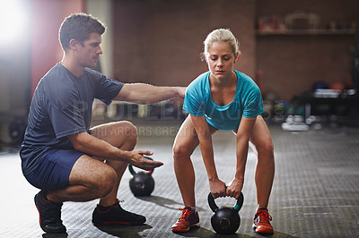 Buy stock photo Shot of a trainer helping a young woman lifting kettlebells in a gym