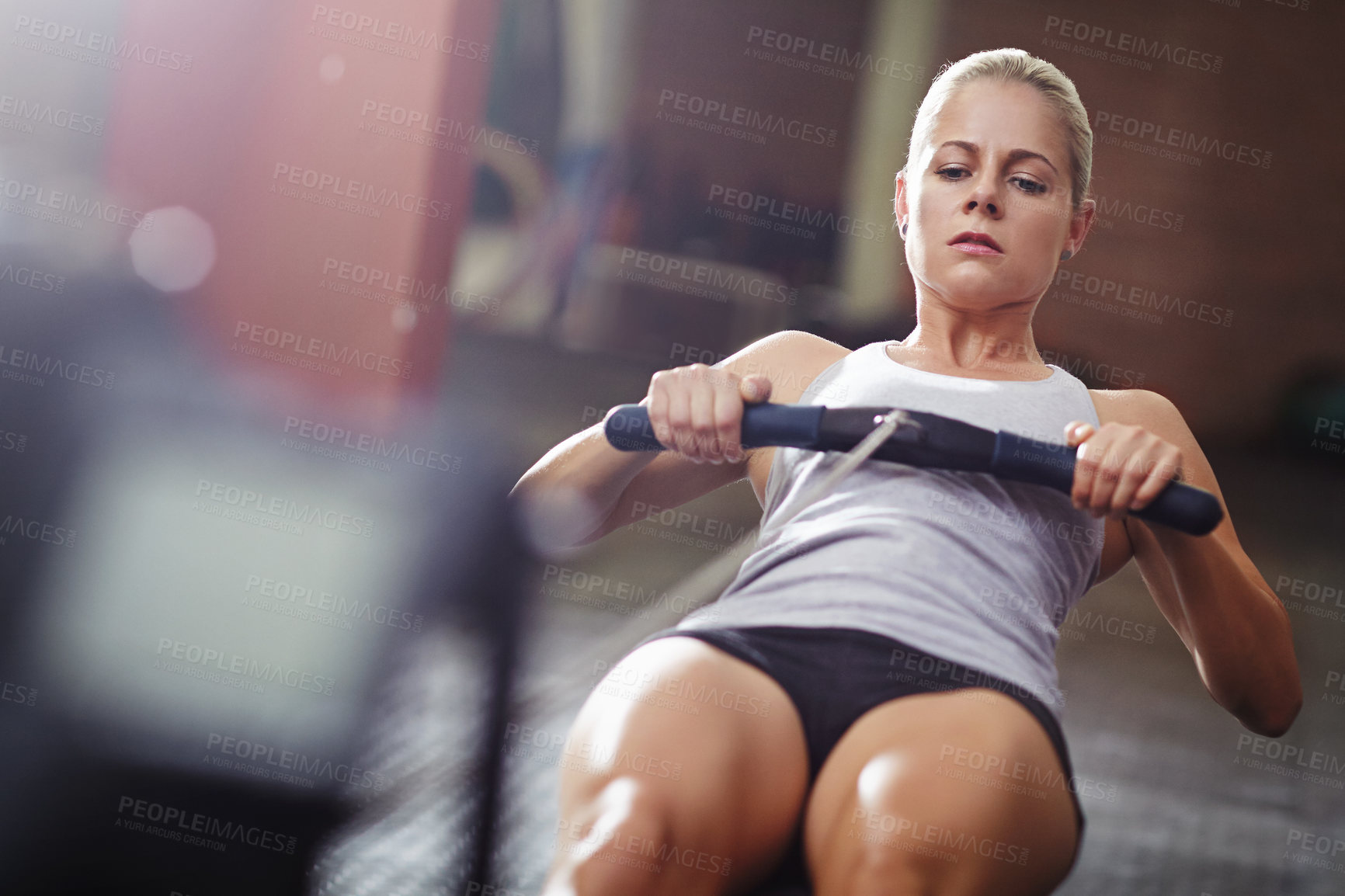 Buy stock photo Shot of a young woman working out on a rowing machine in a gym