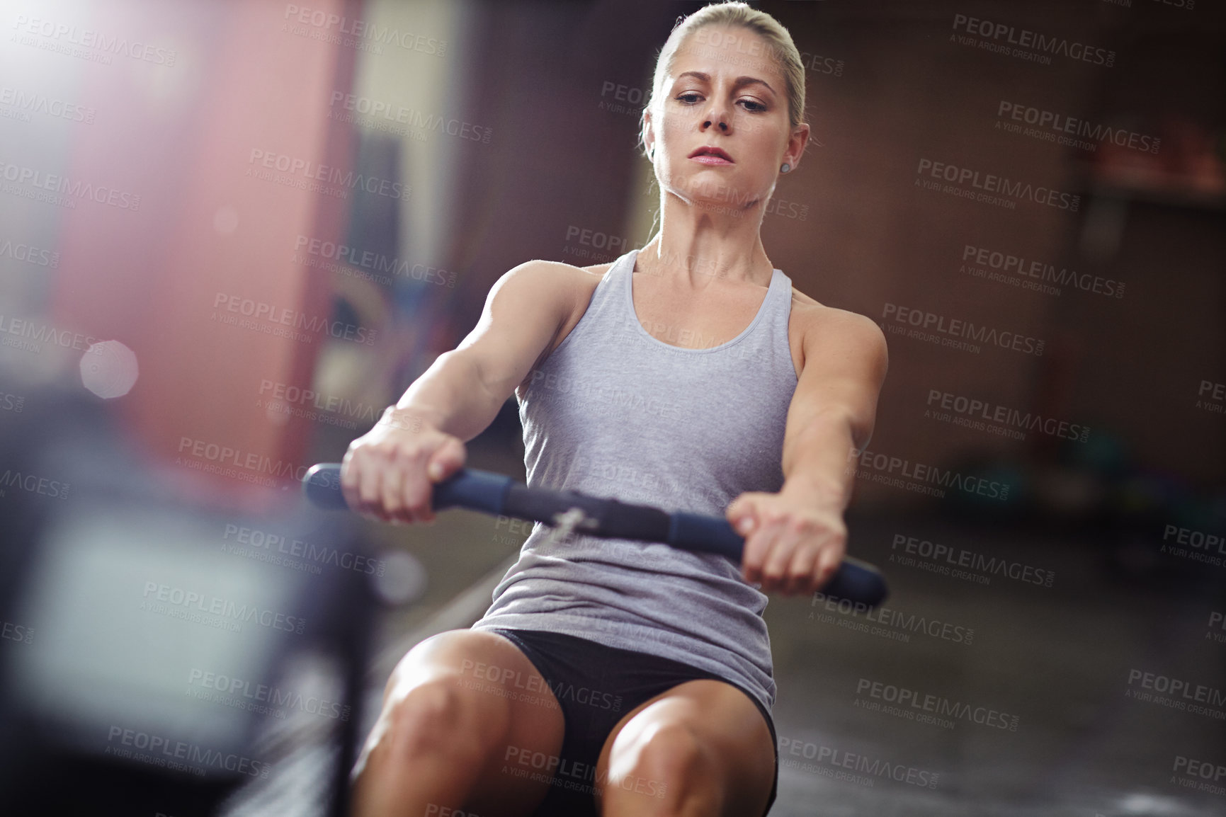 Buy stock photo Shot of a young woman working out on a rowing machine in a gym