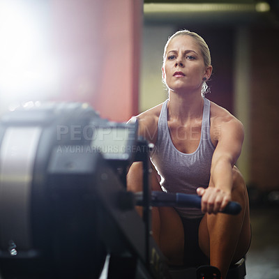 Buy stock photo Shot of a young woman working out on a rowing machine in a gym