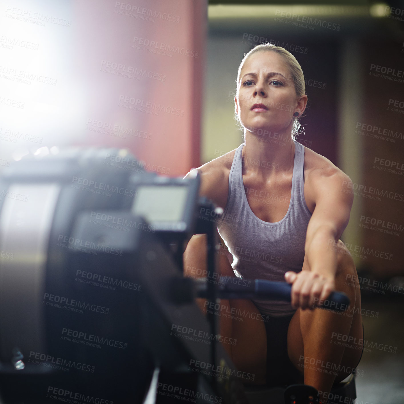 Buy stock photo Shot of a young woman working out on a rowing machine in a gym