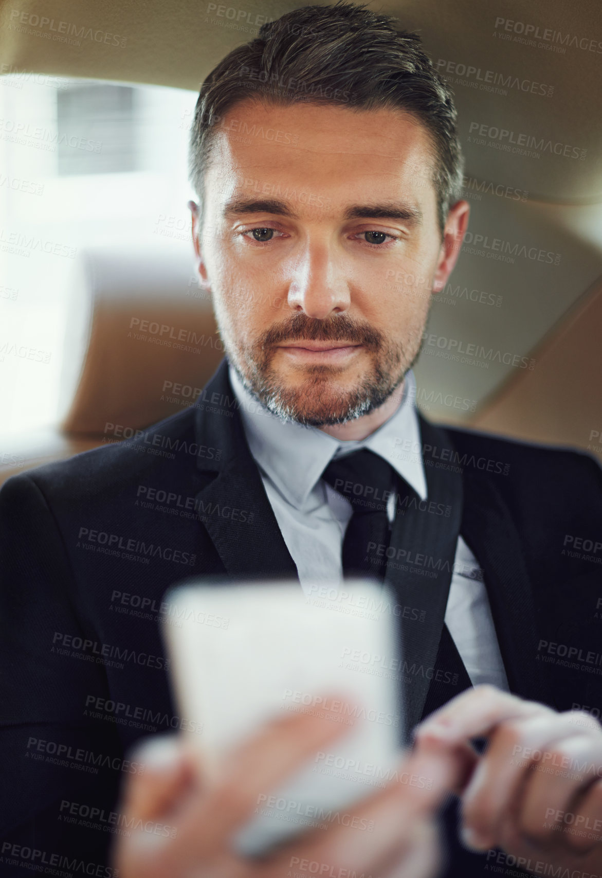 Buy stock photo Cropped shot of a businessman using his cellphone while sitting in the backseat of a car