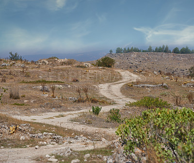 Buy stock photo Landscape view of a lonely dirt road leading out into the mountains during the day. Scenery of a meandering dusty path and trekking trail in a remote and arid area. 