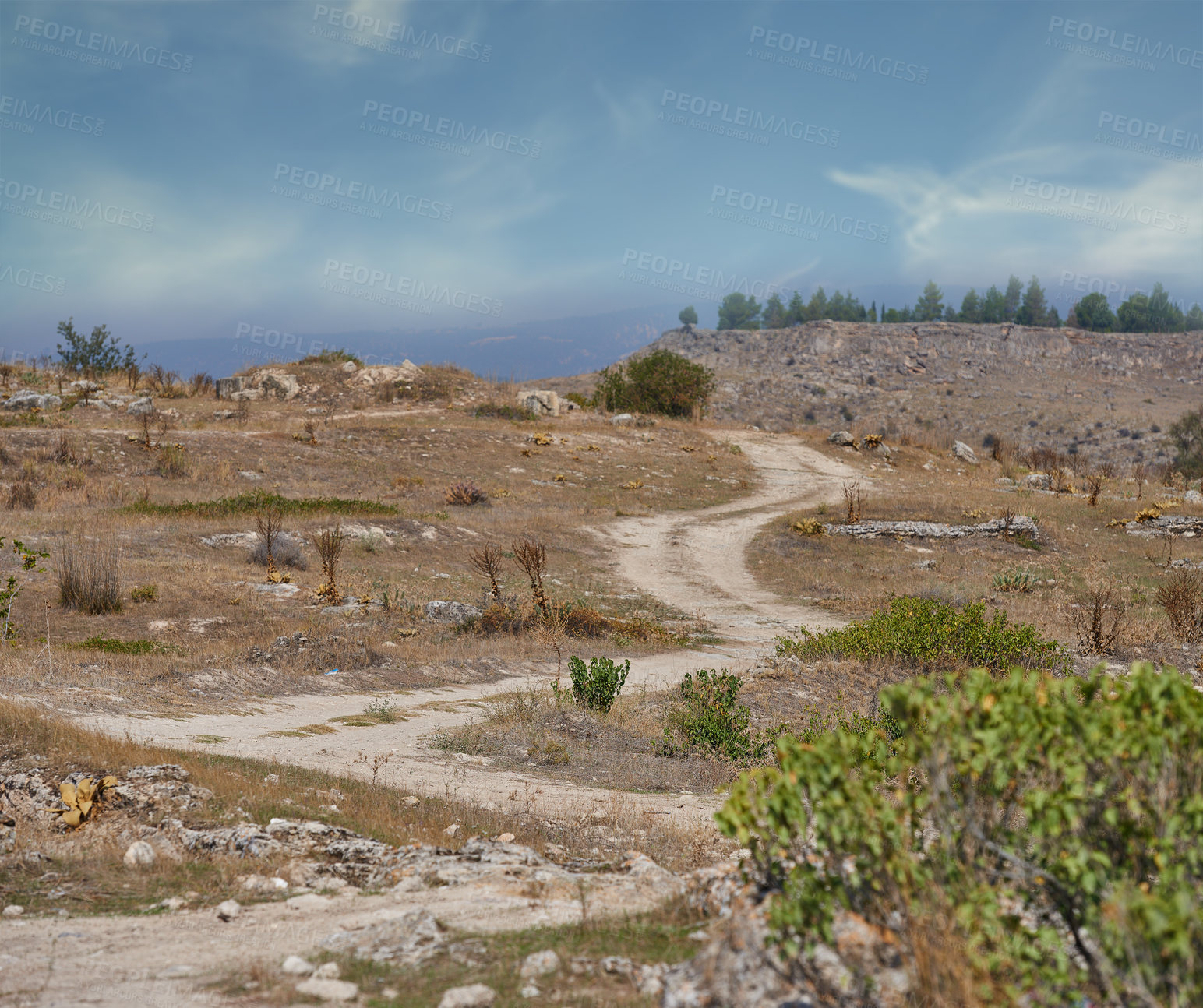 Buy stock photo Landscape view of a lonely dirt road leading out into the mountains during the day. Scenery of a meandering dusty path and trekking trail in a remote and arid area. 