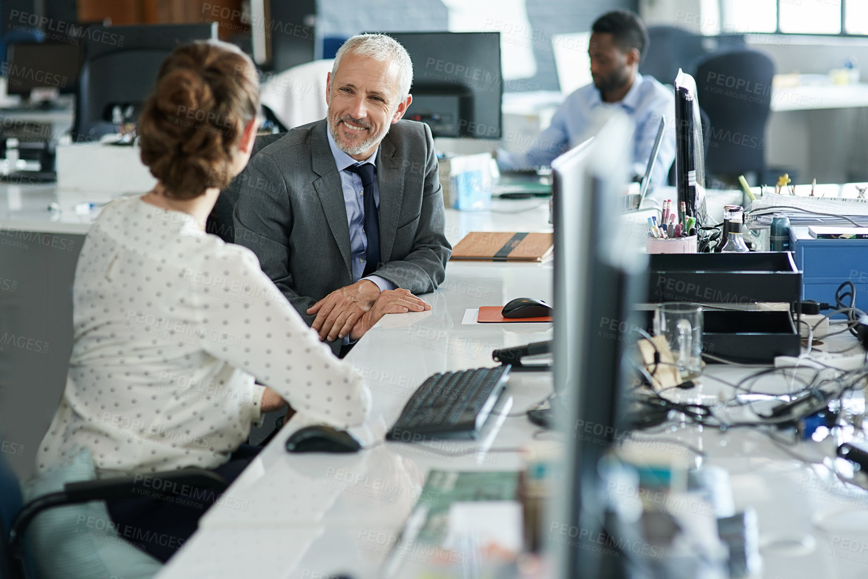 Buy stock photo Shot of two coworkers sitting at their workstations talking together