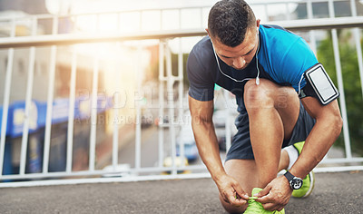 Buy stock photo Shot of a young man tying his shoelaces before a run
