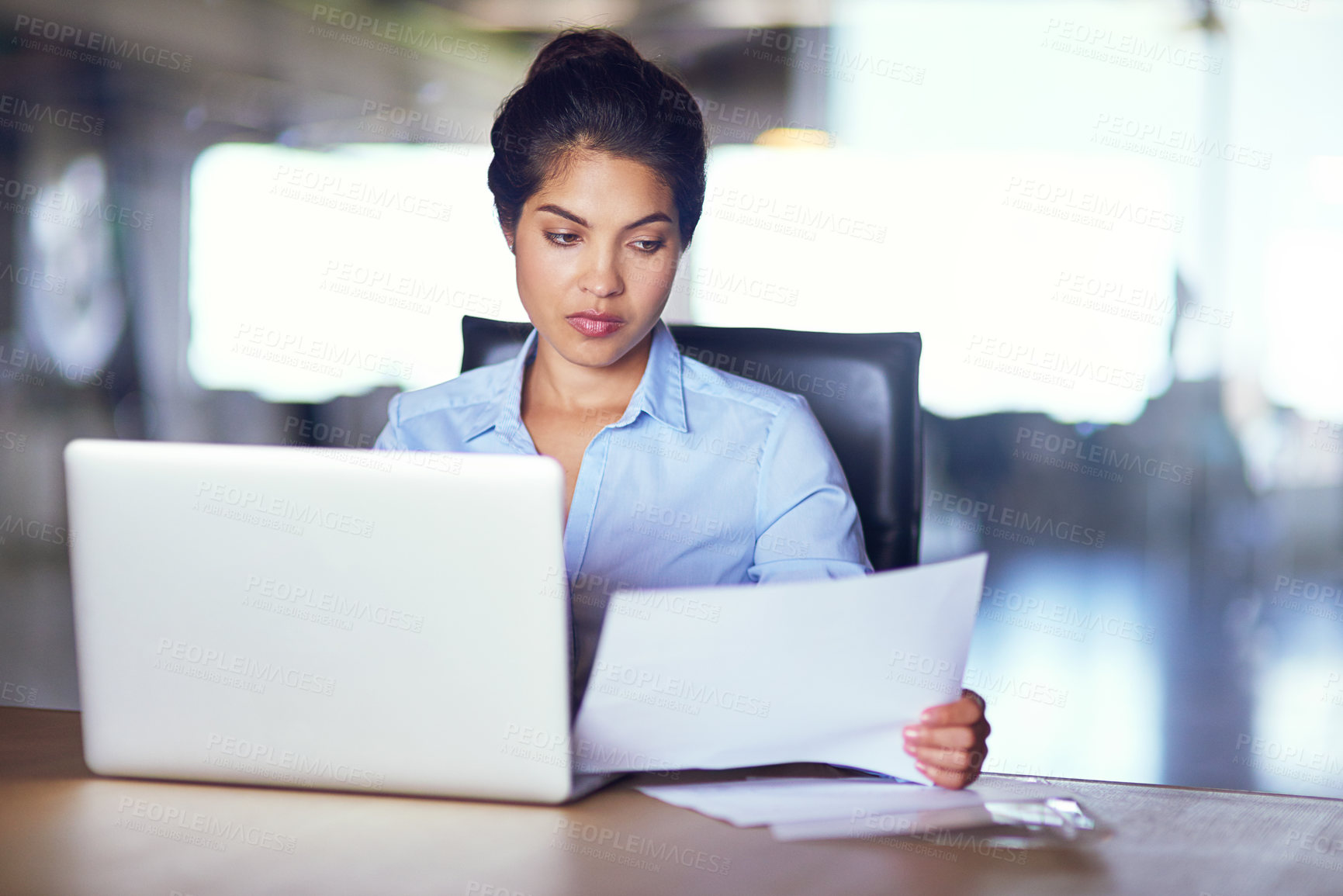 Buy stock photo Shot of a young businesswoman going over documents while working on her laptop
