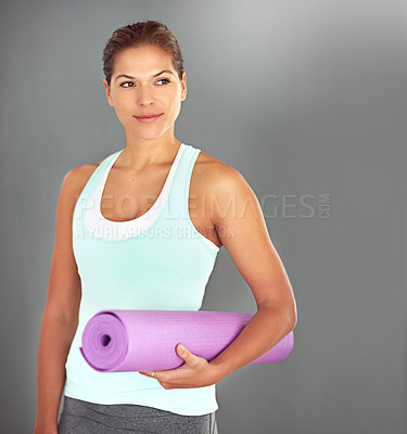 Buy stock photo Shot of a young woman holding a yoga mat while standing against a gray background