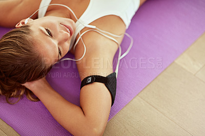 Buy stock photo Cropped shot of a sporty young woman listening to music while lying on an exercise mat