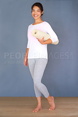 Buy stock photo Full length shot of a sporty young woman holding her yoga mat against a grey background