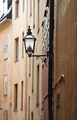 Buy stock photo Cast iron street light in an alley way in a rural town in Europe. Empty street with glass lantern on tall buildings or houses. A hidden side street with traditional architecture and vintage lamp post