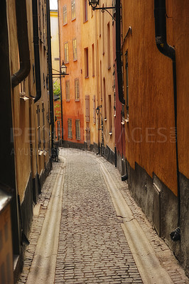 Buy stock photo Quiet, empty cobbled street in a small European tourist city. A narrow alley way in a rural town surrounded by tall apartment buildings or red houses. Hidden side street with traditional architecture