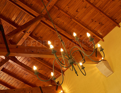 Buy stock photo Below view of an old fashioned chandelier with candle lightbulbs hanging from sturdy wooden roof ceiling inside. Architecture beam detail, interior design, brass, antique light fixture in empty room