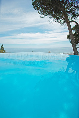 Buy stock photo An outdoor infinity pool with copy space. Low angle of an empty swimming pool with clean, clear water surrounded by green trees and a blue sky. Luxury pool at a holiday resort or tourism guesthouse