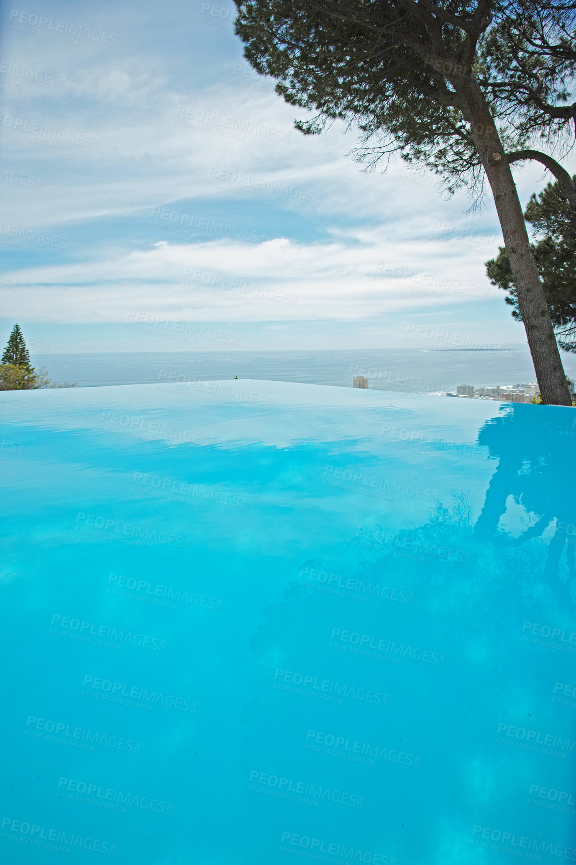 Buy stock photo An outdoor infinity pool with copy space. Low angle of an empty swimming pool with clean, clear water surrounded by green trees and a blue sky. Luxury pool at a holiday resort or tourism guesthouse