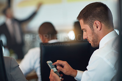 Buy stock photo Cropped shot of a young businessman using his cellphone while sitting in the boardroom