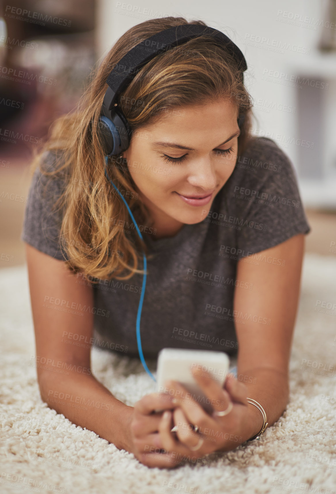Buy stock photo Shot of a young woman relaxing at home and listening to music on her phone