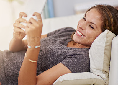Buy stock photo Shot of a young woman relaxing on the sofa with a digital tablet at home