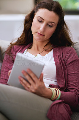 Buy stock photo Cropped shot of a mature woman using her tablet while sitting on the sofa