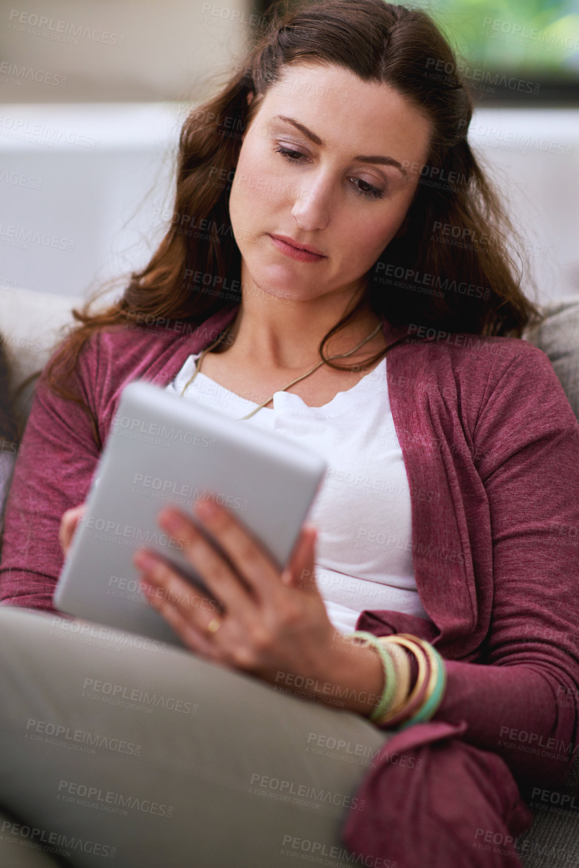 Buy stock photo Cropped shot of a mature woman using her tablet while sitting on the sofa