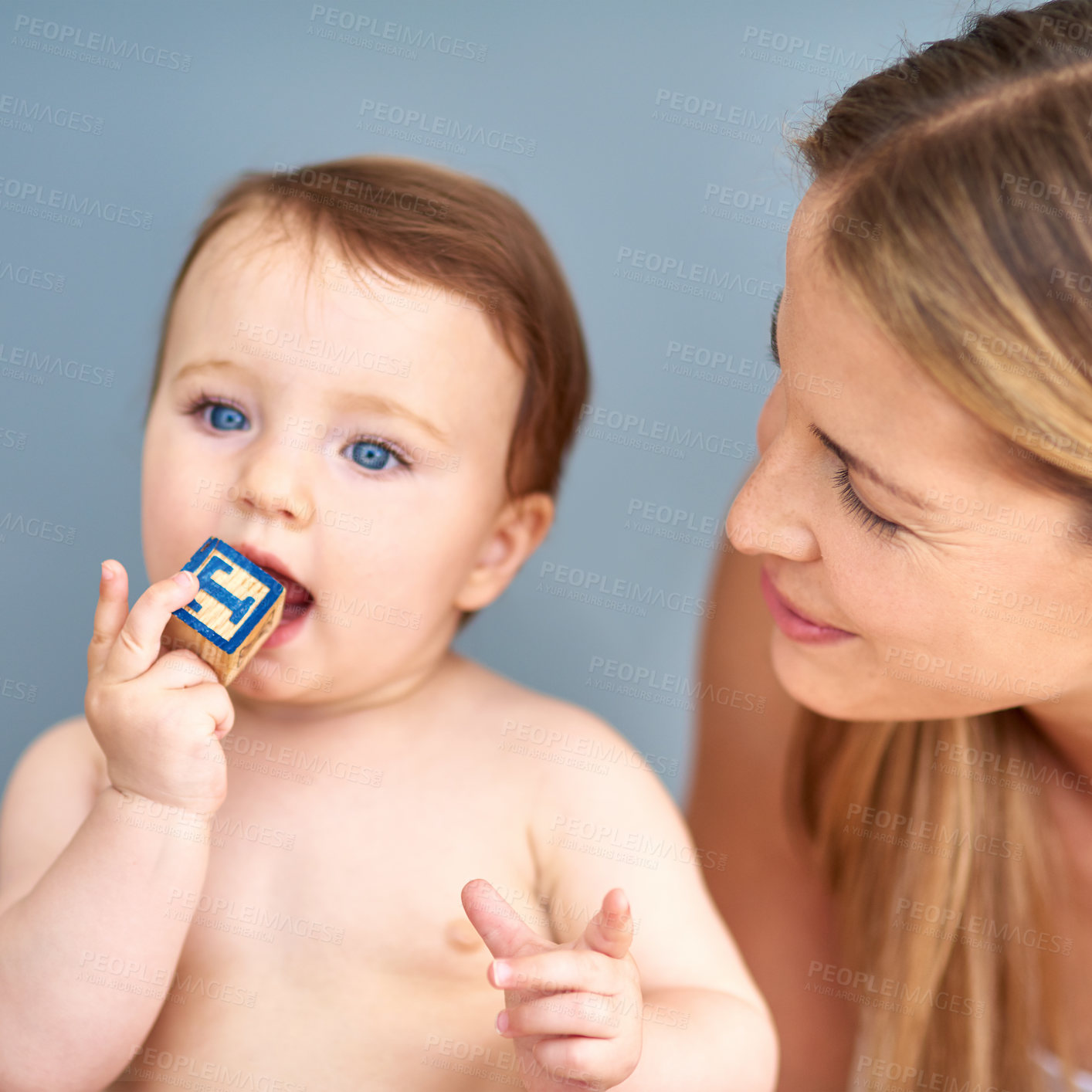 Buy stock photo Shot of an adorable baby girl biting a wooden block while her mother looks on