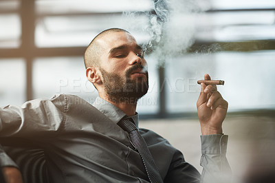 Buy stock photo Shot of a well dressed businessman smoking a cigar in the office
