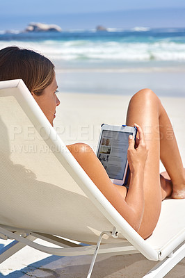 Buy stock photo Cropped shot of a young woman using her tablet while relaxing at the beach