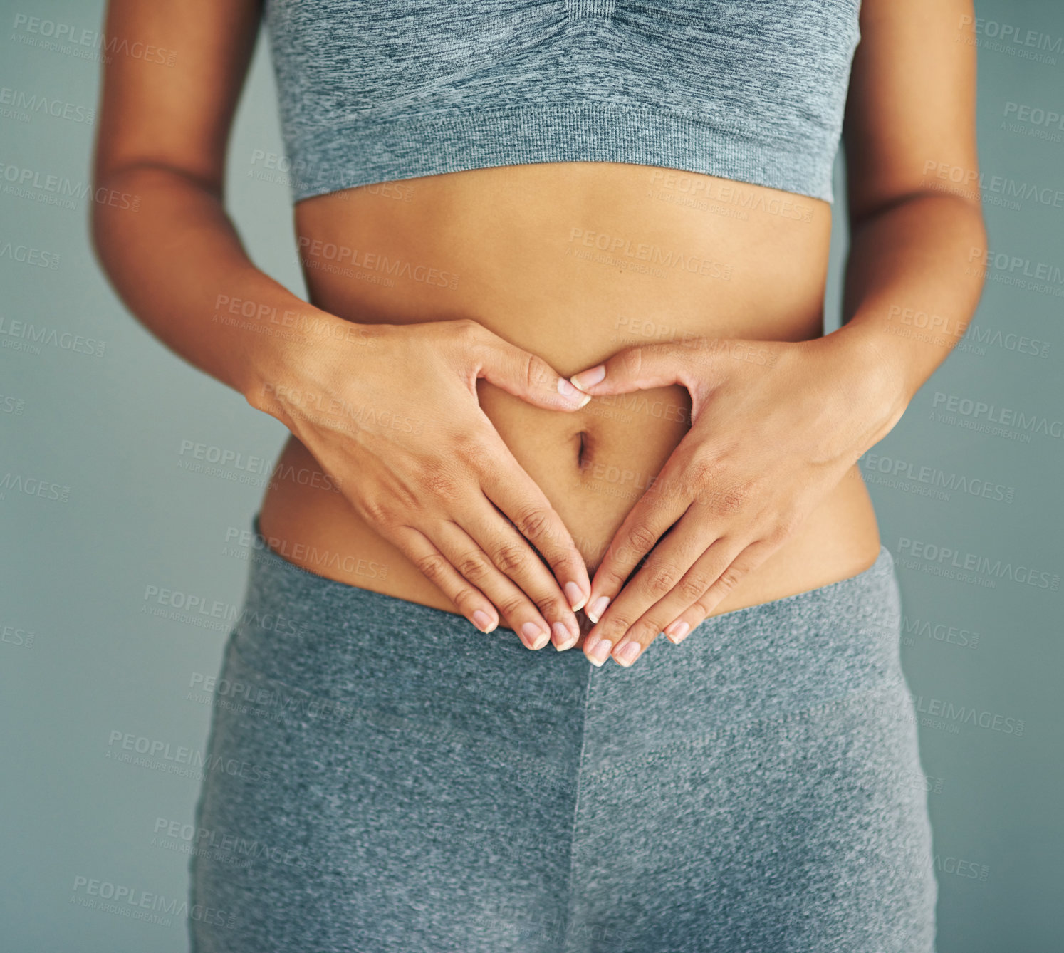 Buy stock photo Cropped shot of a young woman making a heart shape on her stomach