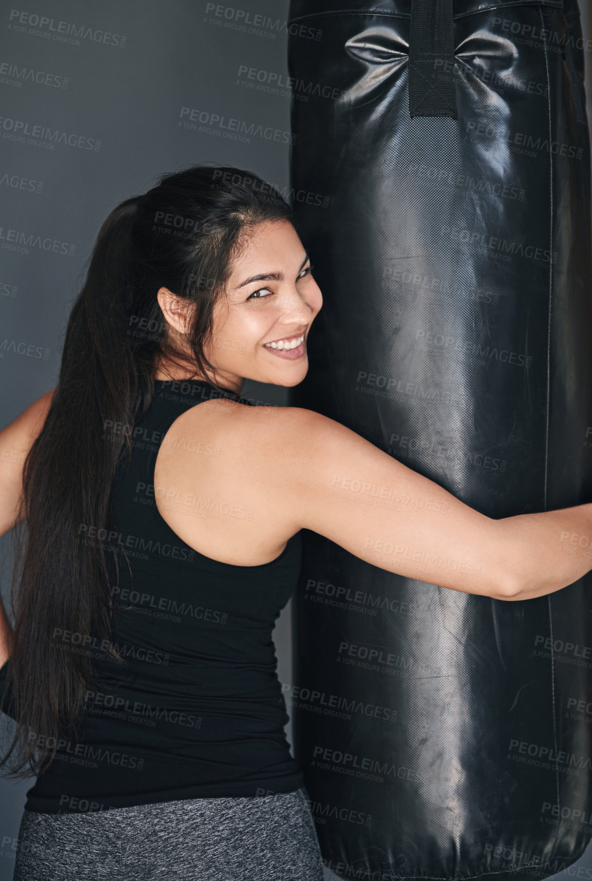 Buy stock photo Woman, portrait and punching bag in studio for fitness, cardio boxing and building endurance for strength. Girl, happy and gray background for self defense, adrenaline control and combat training.