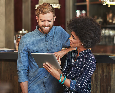 Buy stock photo Shot of a young man and woman using a digital tablet together at a cafe