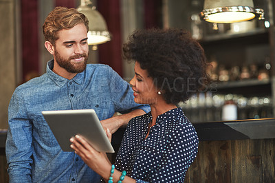 Buy stock photo Shot of a young man and woman using a digital tablet together at a cafe