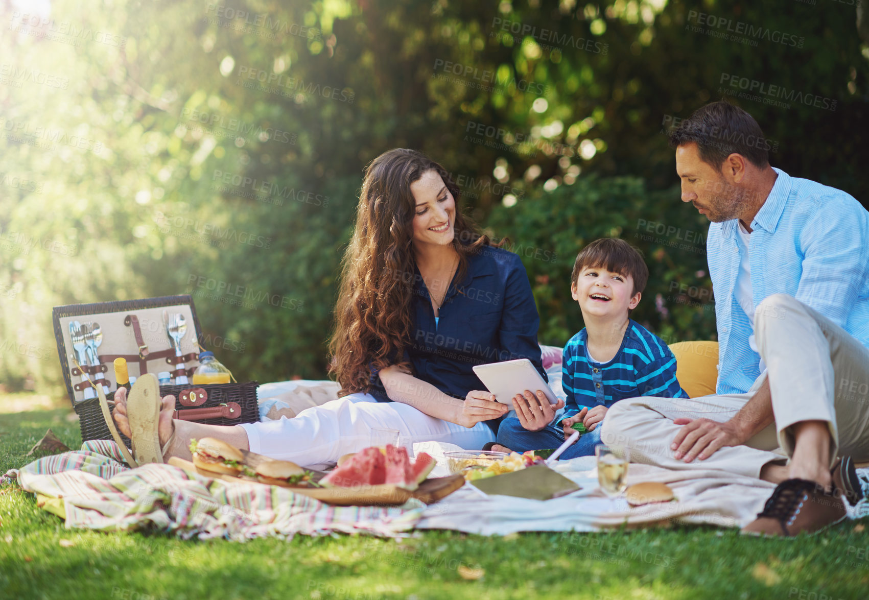Buy stock photo Shot of a young family using a digital tablet during a picnic in the park
