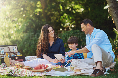 Buy stock photo Shot of a young family using a digital tablet during a picnic in the park