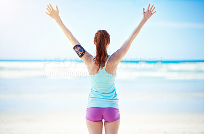 Buy stock photo Rearview shot of a young woman standing with her arms outstretched on the beach