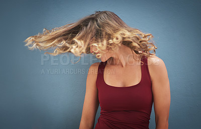 Buy stock photo Shot of a young woman twirling her hair against a gray background
