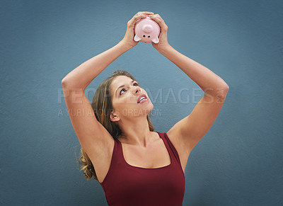Buy stock photo Shot of a young woman holding a piggybank in the air against a gray background