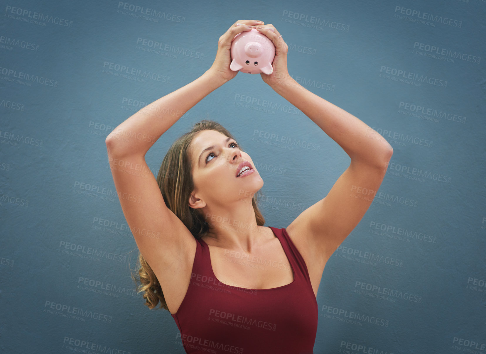 Buy stock photo Shot of a young woman holding a piggybank in the air against a gray background