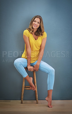 Buy stock photo Shot of a young woman sitting on a chair against a gray wall