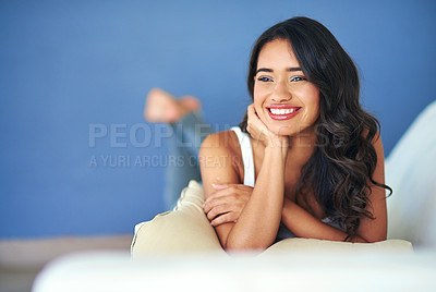 Buy stock photo Shot of a young woman looking thoughtful while lying on her living room sofa