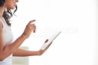 Buy stock photo Cropped shot of a young woman using her tablet while sitting in her living room