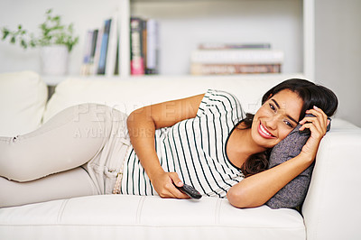 Buy stock photo Portrait of woman laying on sofa, tv remote and watching tv with smile on face in living room. Time to relax, streaming movie bright home, happy woman on couch with television in lounge in India.