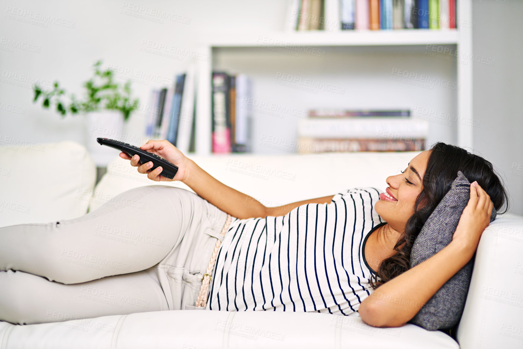 Buy stock photo Cropped shot of a young woman watching TV while relaxing on her sofa at home