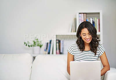 Buy stock photo Cropped shot of a young woman using her laptop while relaxing on her sofa at home