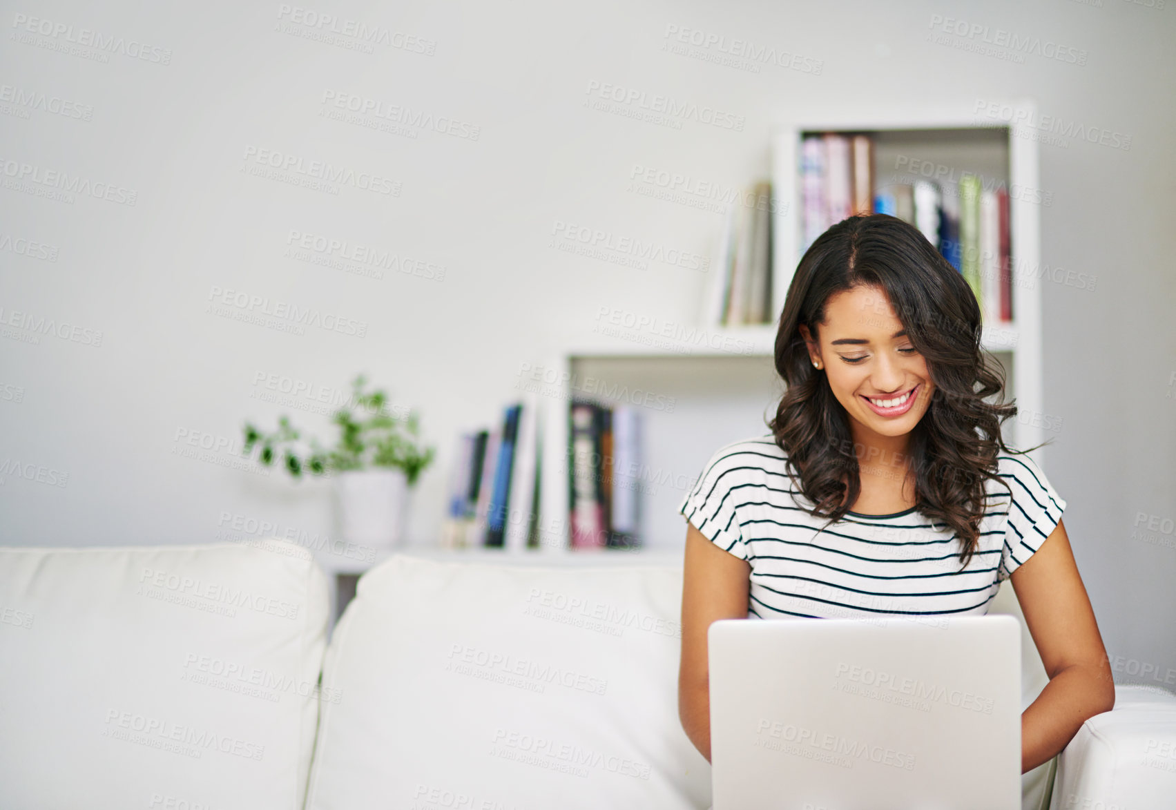 Buy stock photo Cropped shot of a young woman using her laptop while relaxing on her sofa at home